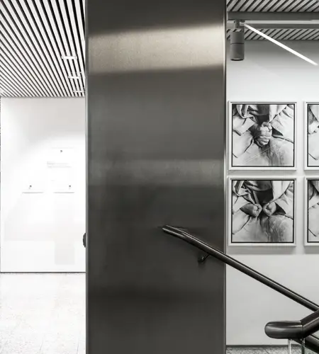 We look into the Vertikale Galerie in Vienna. We see a staircase decorated in light tones. Photographs are displayed on the walls.