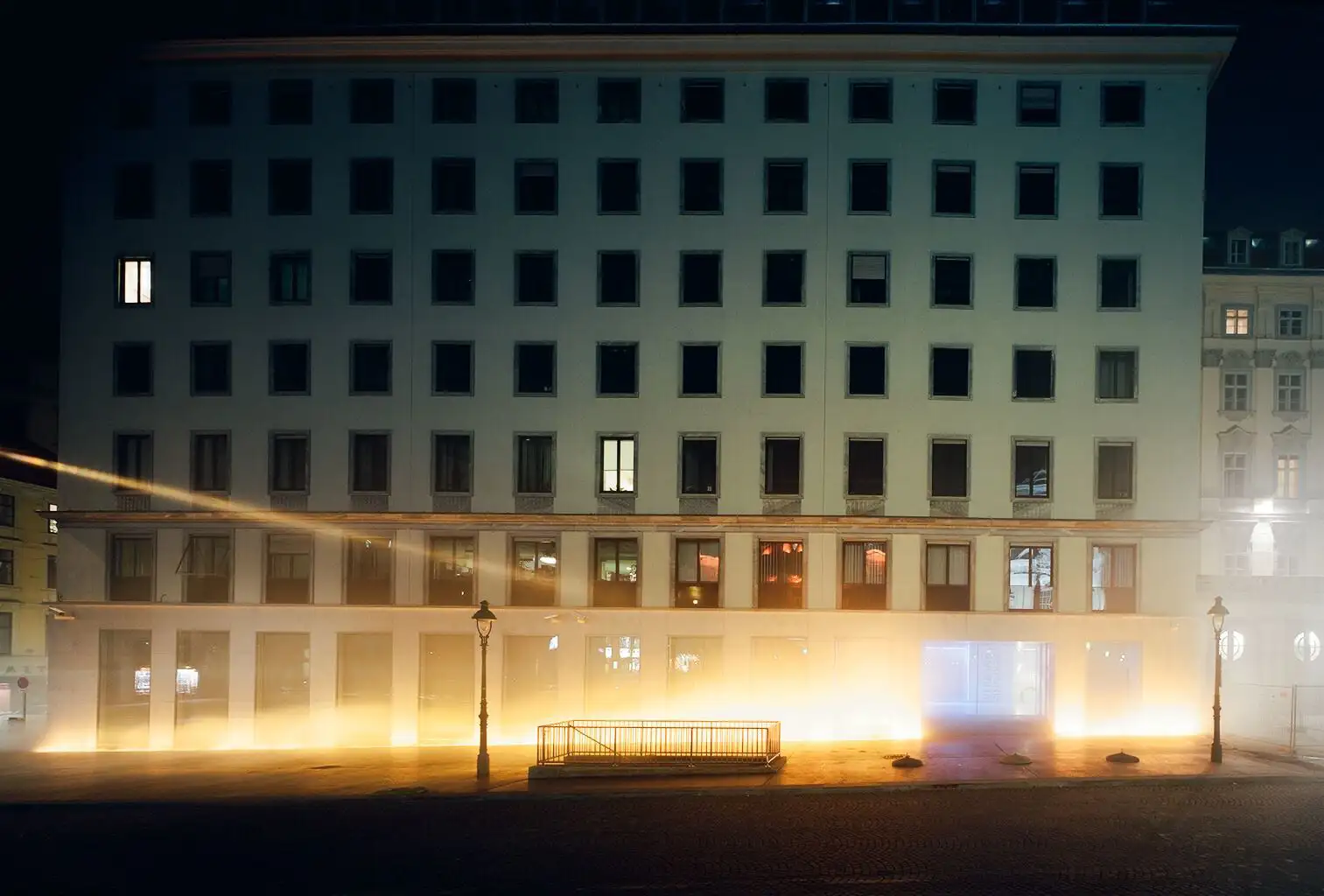 View of the VERBUND building in the courtyard. It is dark and Olafur Eliasson's installation transforms the square and the building into a stage of fog, light and wind.