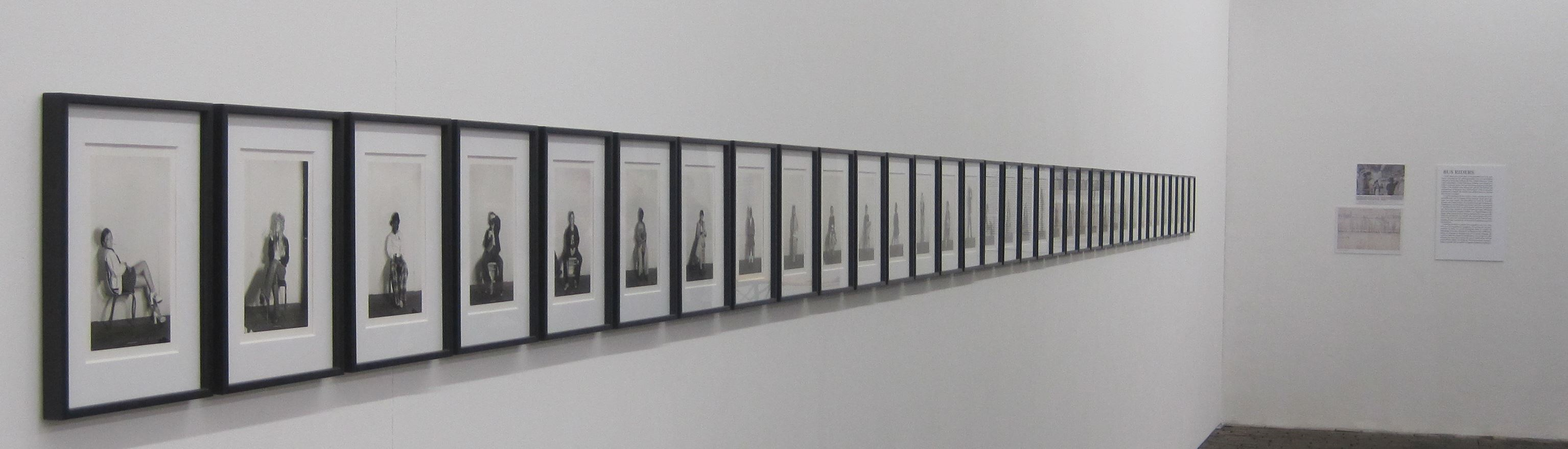 Sequence of framed black-and-white photographs on a white wall in an art gallery, depicting a series of portraits.