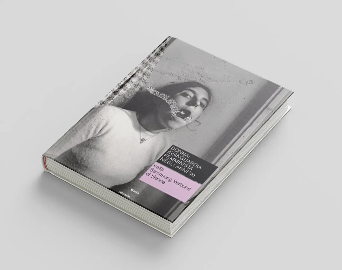 The exhibition catalog for the Feminist Avant-Garde exhibition in Rome shows a black and white portrait of a dark-haired woman in front of a gray wall. She is wearing knitting and deconstructed water bubbles come out of her mouth.