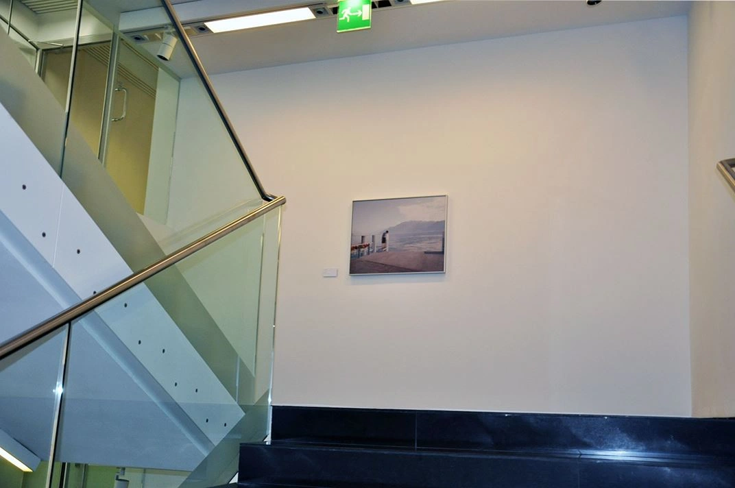 Treppenaufgang mit modernem Design, ausgestattet mit Glasgeländer und einer Wand mit einem gerahmten Bild einer Industrielandschaft in einem Bürogebäude.