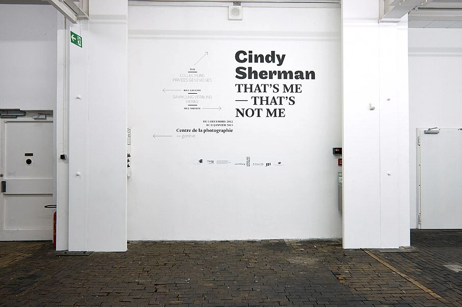 Eingangsbereich der Cindy Sherman Ausstellung mit dem Titel "That's me – That's not me" an der Wand einer Galerie mit hellem Innenraum und Kopfsteinpflasterboden.