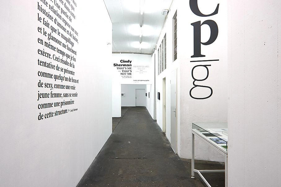 Corridor of an art gallery with text on the walls and directional signs to the Cindy Sherman exhibition "That's me – That's not me."