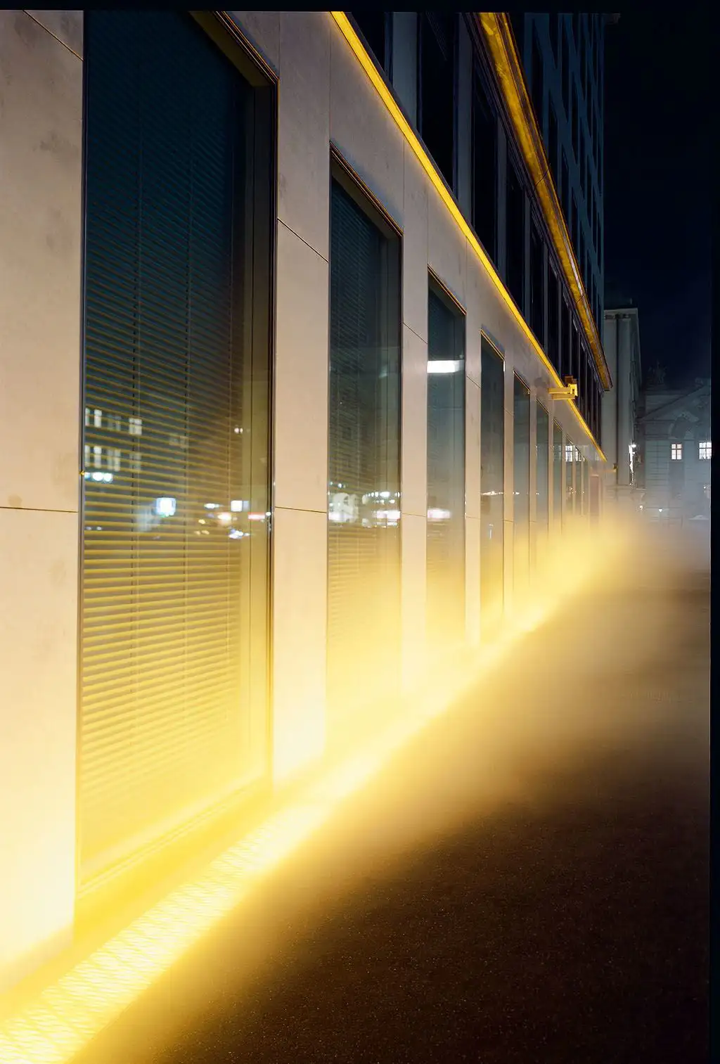 View of the VERBUND building in the courtyard. It is dark and Olafur Eliasson's installation transforms the square and the building into a stage of fog, light and wind.