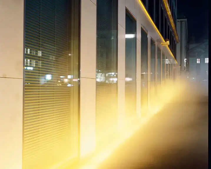 View of the VERBUND building in the courtyard. It is dark and Olafur Eliasson's installation transforms the square and the building into a stage of fog, light and wind.