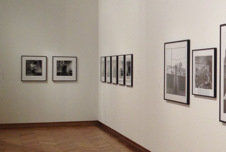 Innenansicht einer Fotogalerie mit einer Auswahl von gerahmten Schwarz-Weiß-Fotografien, die chronologisch an einer weißen Wand hängen, in einem Raum mit Holzboden und sanfter Beleuchtung.