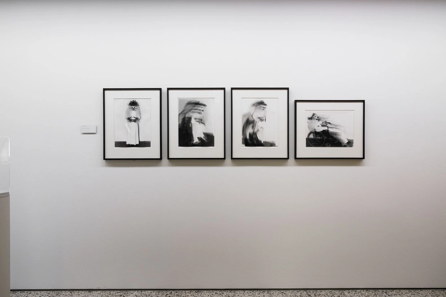 A series of four black and white portrait photographs in black frames on a white wall in a gallery.