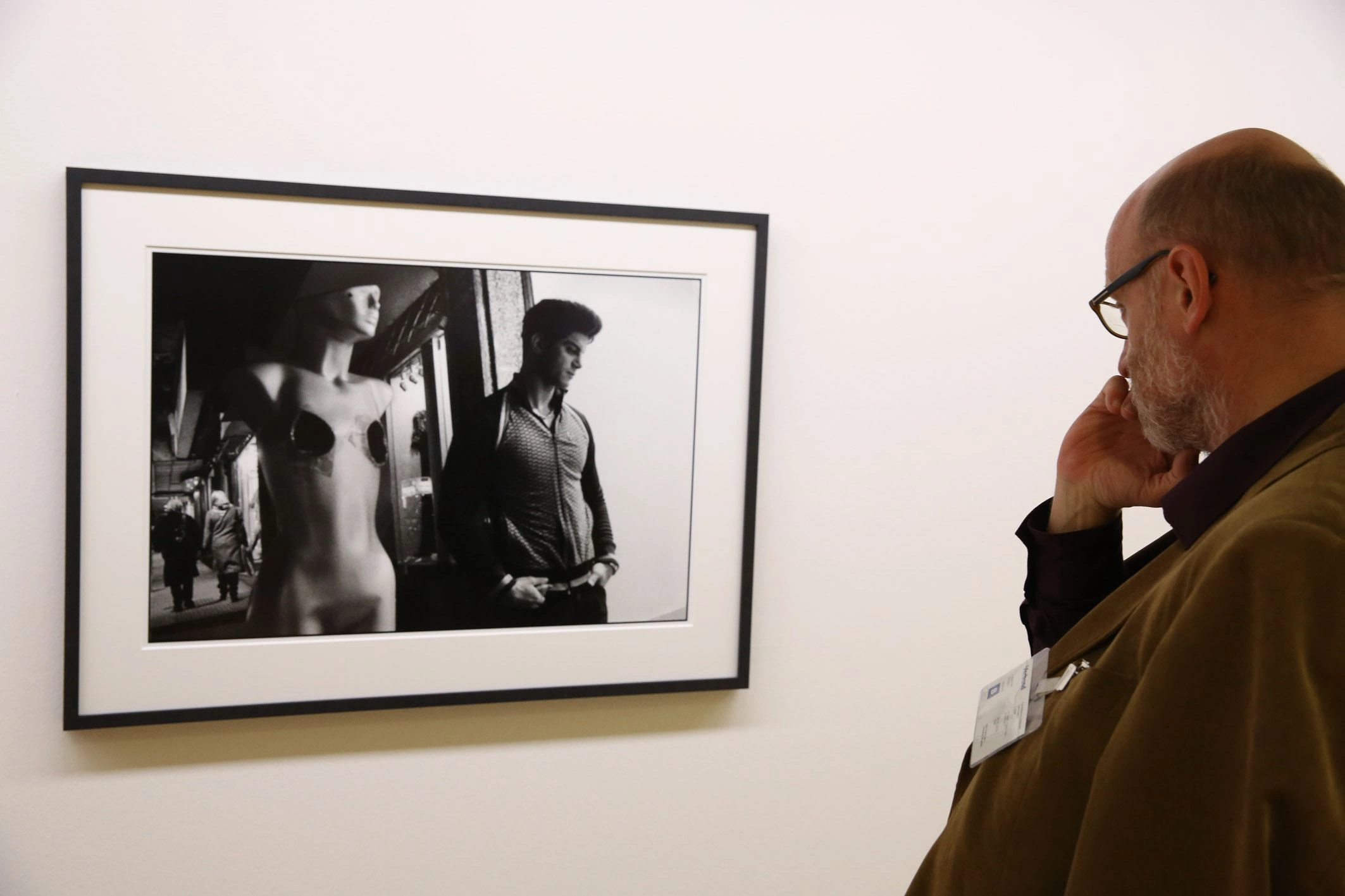 Zu sehen ist eine schwarz weiße Fotographie auf einer weißen Wand. Ein Mann steht rechts davon und betrachtet nachdenklich das Kunstwerk.