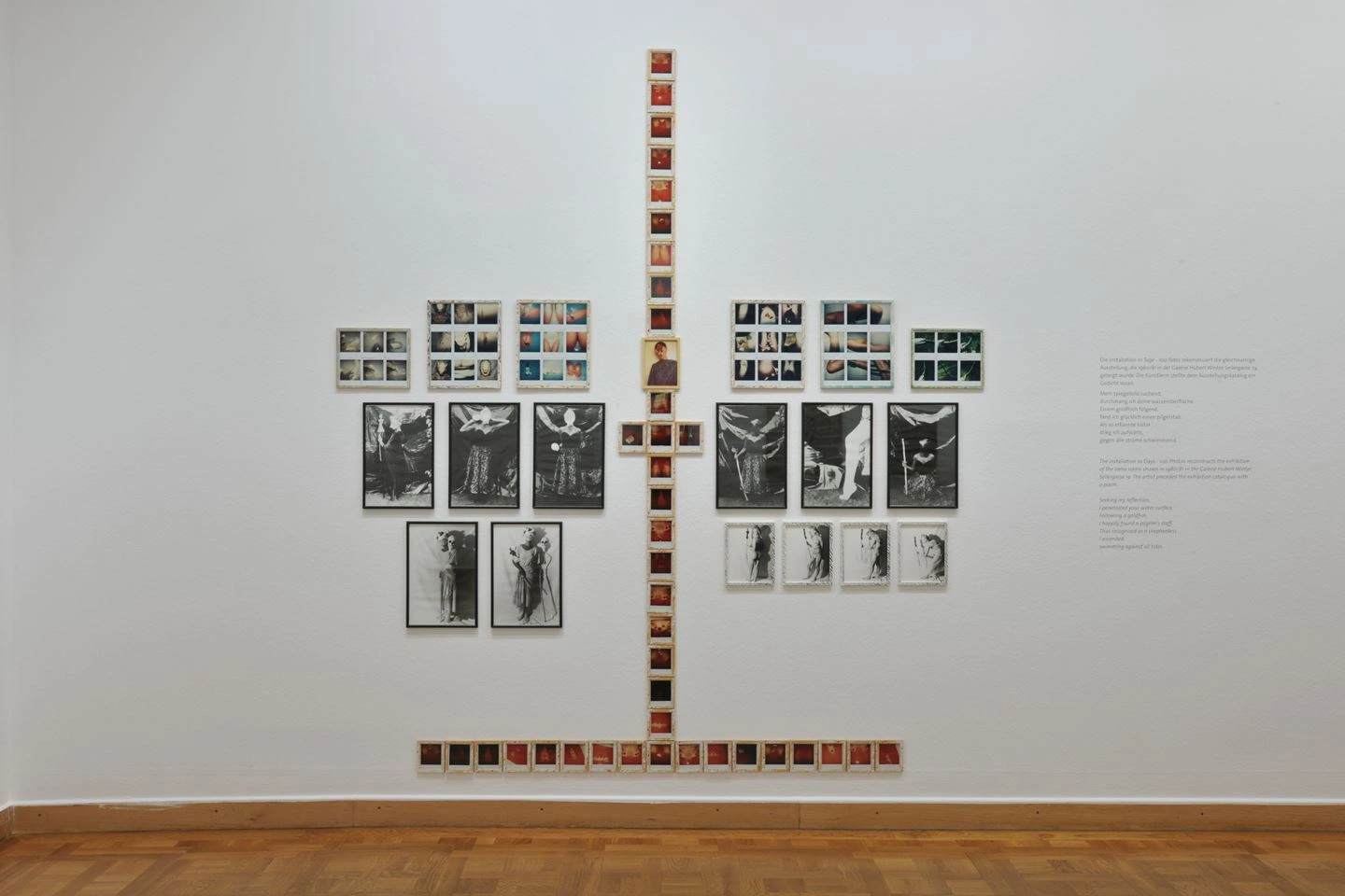 An exhibition hall with white walls showcases a creative arrangement of black-and-white photographs arranged in two vertical rows with a horizontal connection in the middle, forming a cross-like pattern.