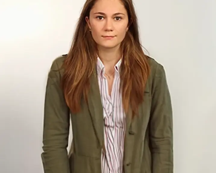 Sophie Rueger stands in front of a light-colored wall. A smile plays around her lips.