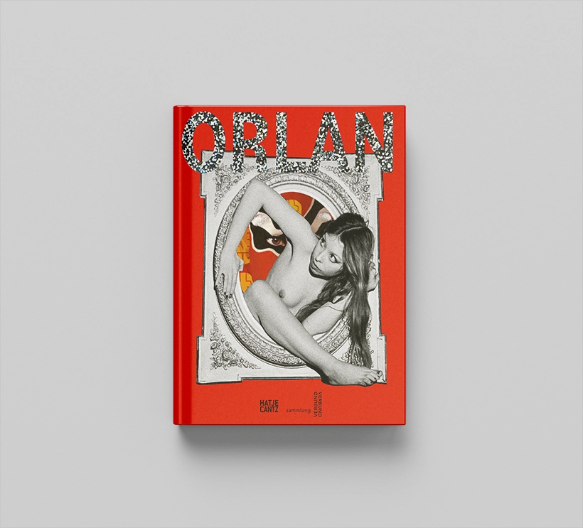 The artist ORLAN's exhibition catalog lies on a gray background. This is mostly red. The cover is a black and white photograph of the artist in her younger years. She is naked and frees herself from a frame. The word ORLAN is written above it in glittering letters.