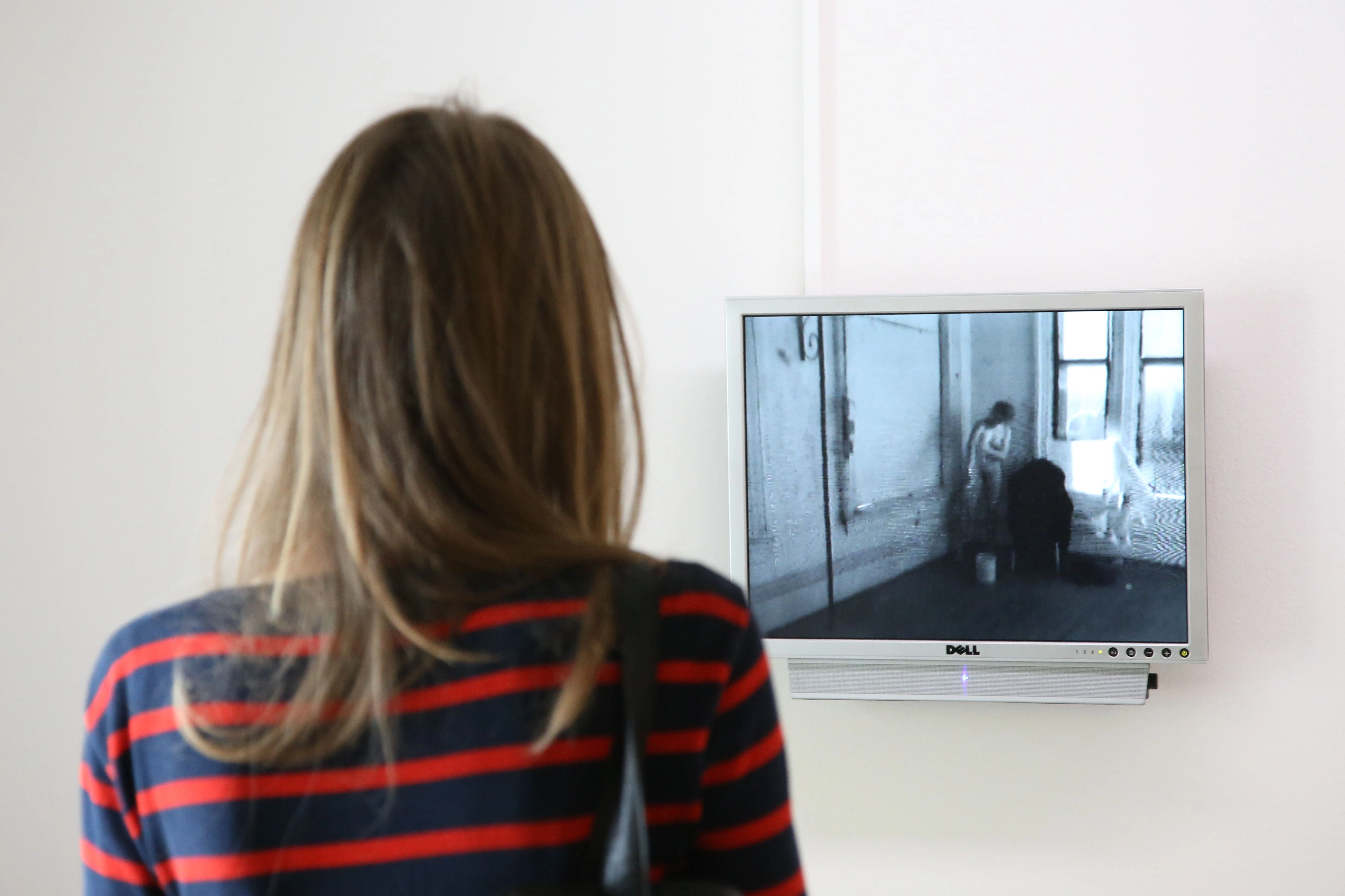 A visitor with a striped top watches a video on a screen hanging on a white wall.