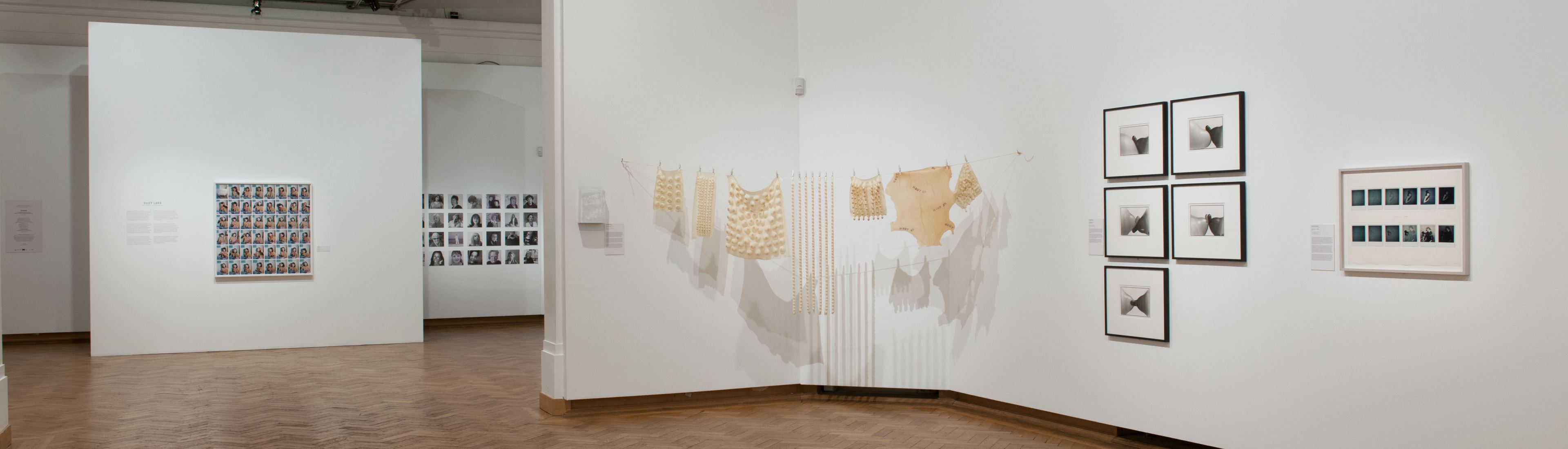 Zu sehen ist ein Ausstellungsraum mit mehreren Kunstwerken von Bozar. Es hängen unterschiedliche Bilderrahmen an den Galleriewänden. Außerdem ist eine Leine gespannt an der Gegenstände hängen.