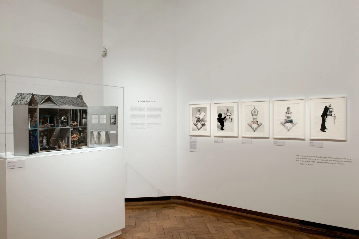 In einem Ausstellungsraum der Ausstellung von Bozar in Brüssel befindet sich rechts eine Vitrine mit einem Modell eines Hauses dessen Innenleben sichtbar ist. Rechts befinden sich auf einer weißen Wand fünf Fotographien in weißen Bilderrahmen.