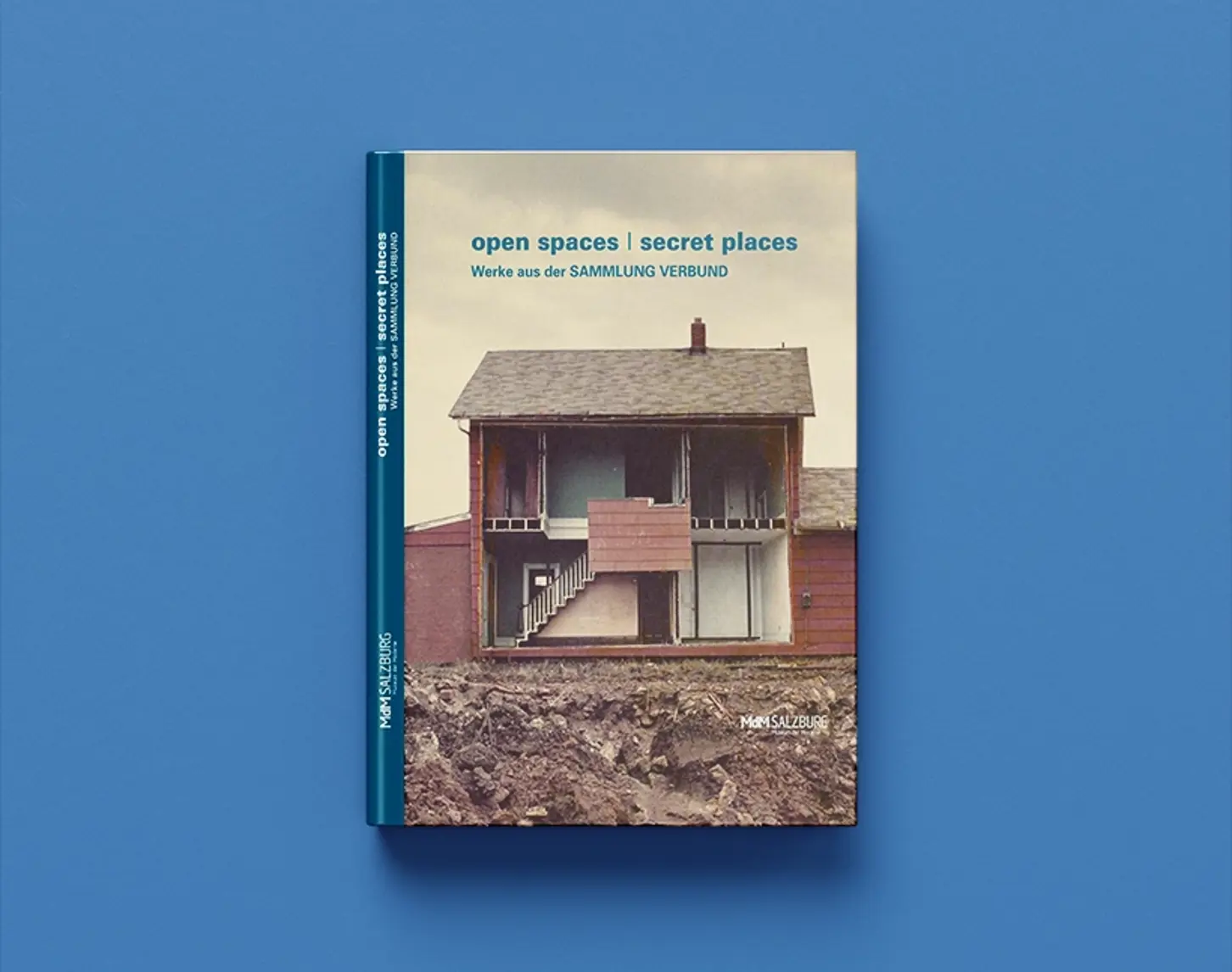 We see the exhibition catalog of open spaces / secret places from 2012. The cover shows direct insights into a single-family home. A side wall was removed so that the viewer can see into the interior of the house.