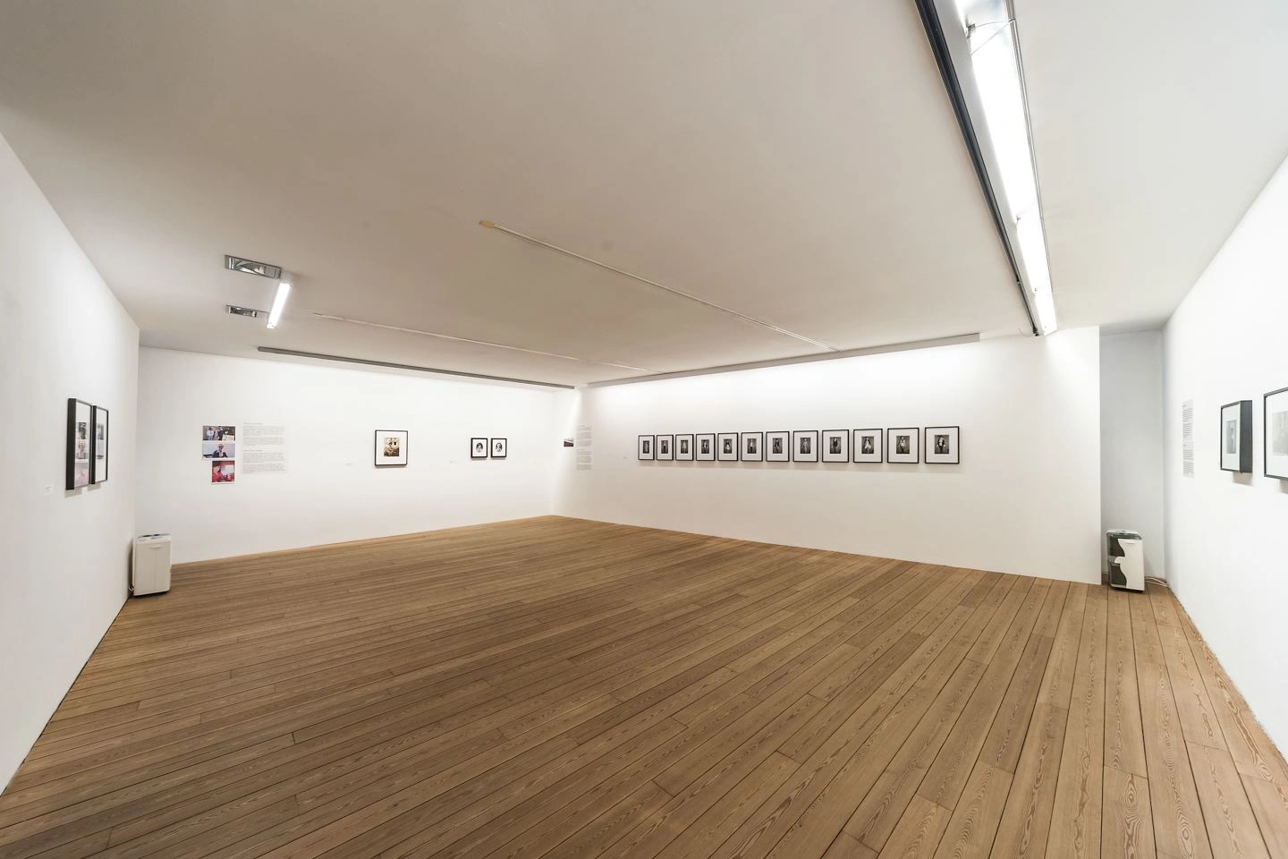 Ein Ausstellungsraum wird aus der Ecke großflächig gezeigt. An jeder Wand hängen kleinformatige Kunstwerke. In zwei Ecken stehen zwei kleine Objekte.