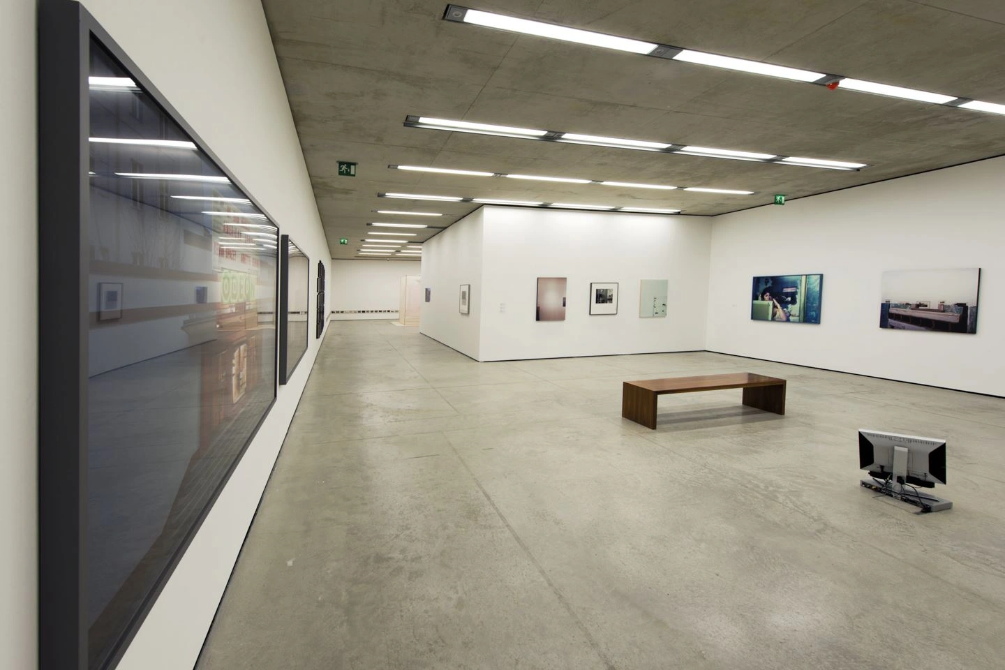 Spacious gallery room with modern art on the walls, a central seating option, and uniform ceiling lighting on smooth concrete flooring.