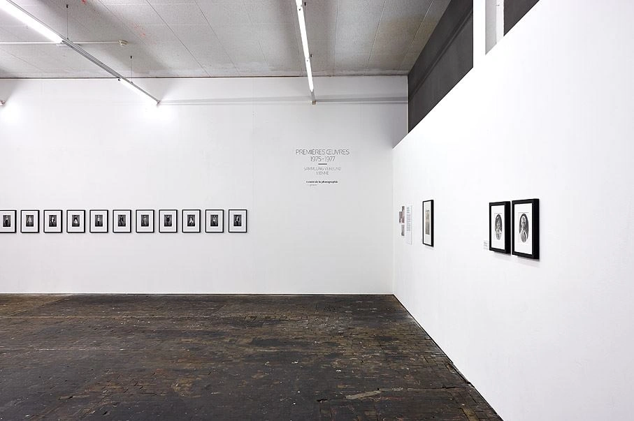 Contemporary art gallery featuring a row of black and white portrait photographs on a white wall with dark wooden flooring.