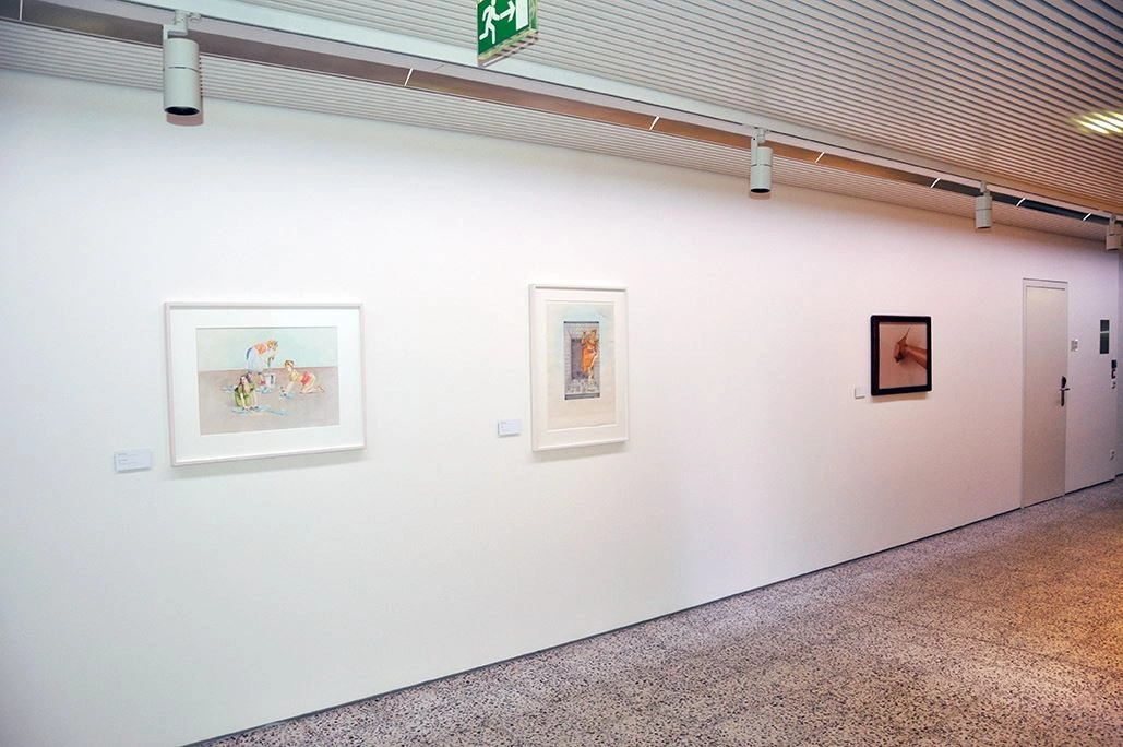 Interior view of an art gallery with a white hallway featuring three different framed pictures, artistic lighting overhead.