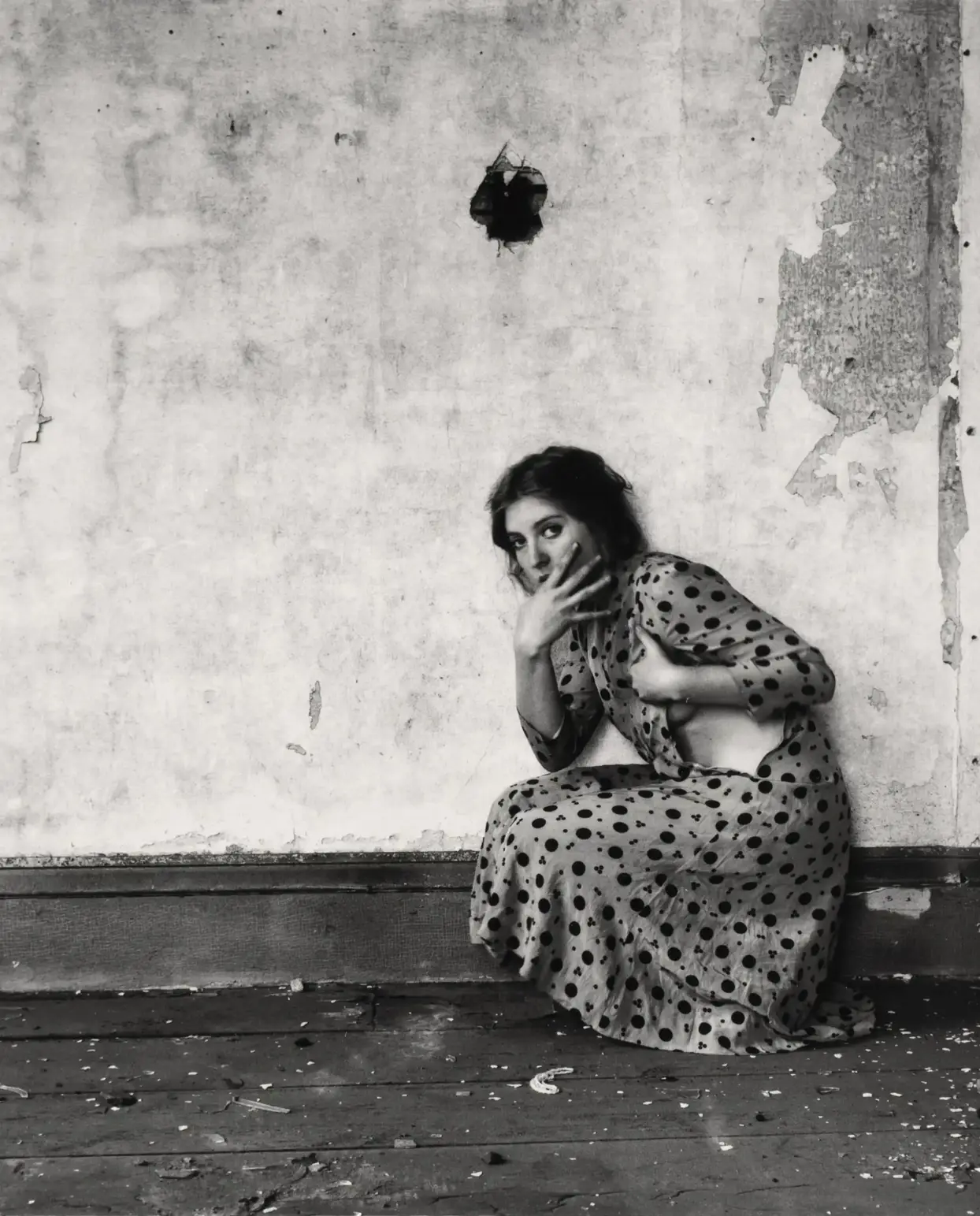 Francesca Woodman's work with the polka dot from 1976 shows a woman in front of a desolate backdrop: Old wooden floor, the plaster crumbling from the defective wall. She crouches on the floor and looks into the camera. She is wearing a polka-dot dress. It is ripped open at the side and discreetly shows off her body.