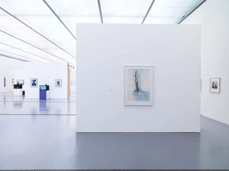 An exhibition room in bluish light with a blue floor can be seen, and paintings hang on several walls, all in blue clay.