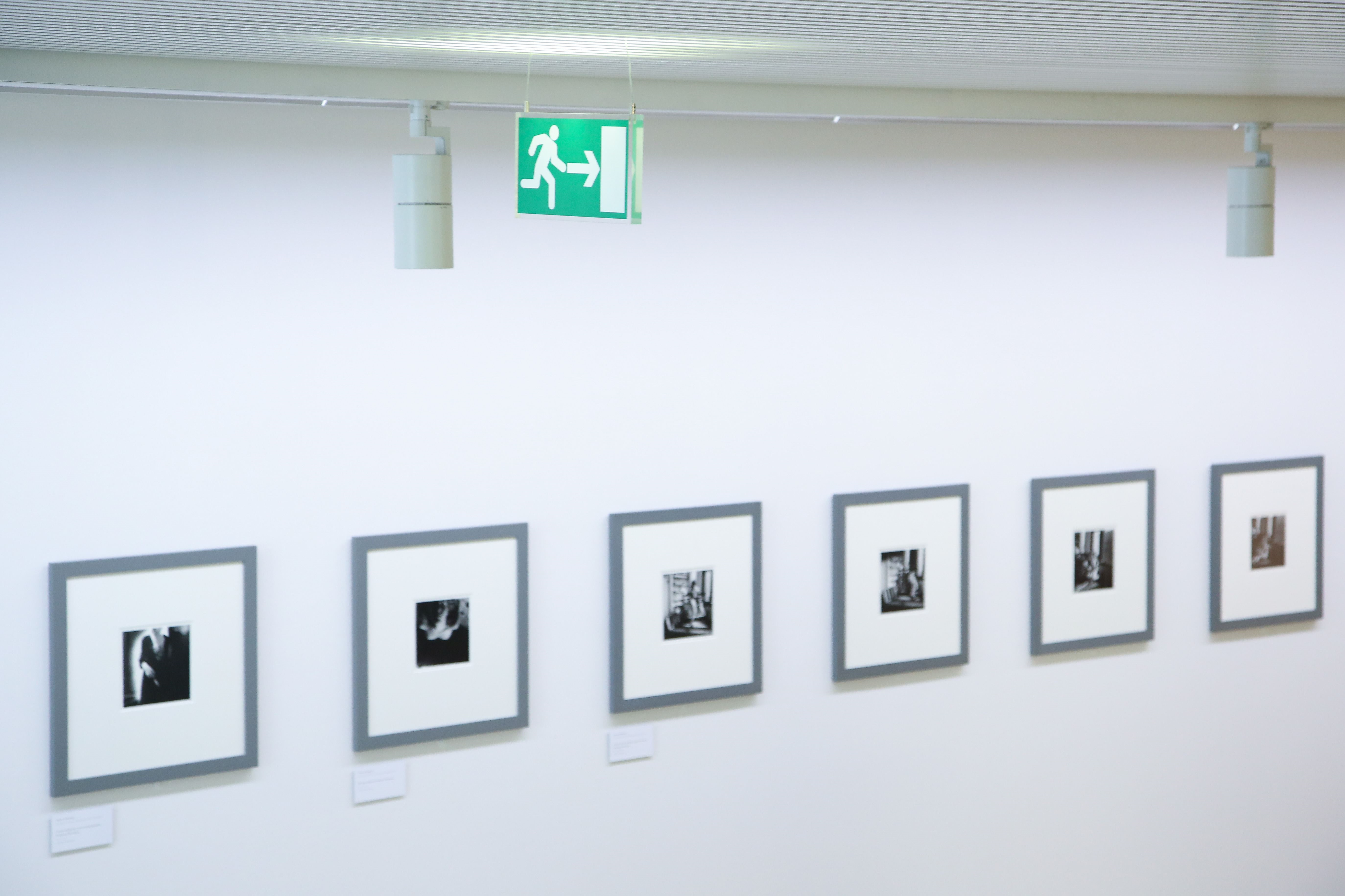 Six square pictures with silver frames hang in a row on a white wall. They are black and white photographs in a passe-partout frame.